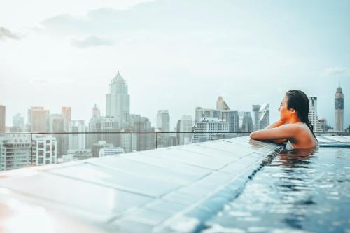 a woman in a infinity pool with a view of a city at Column Bangkok Hotel in Bangkok
