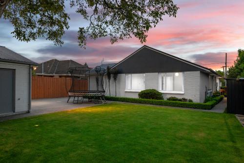 uma casa com um jardim verde com um banco em Family-Friendly, Airport 6 mins, Spacious with Garden em Christchurch