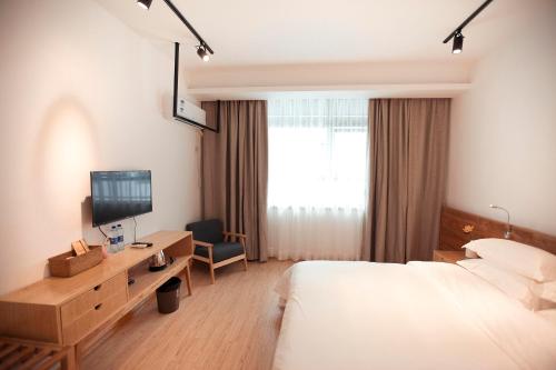 a hotel room with a bed and a desk with a television at Zhangjiajie One Art Guesthouse in Zhangjiajie