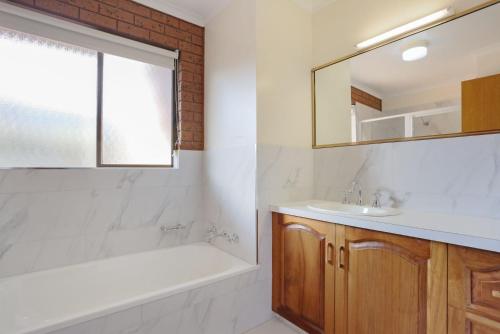 ein Badezimmer mit einer Badewanne, einem Waschbecken und einem Spiegel in der Unterkunft Unit 6 11 Beach Street Merimbula in Merimbula