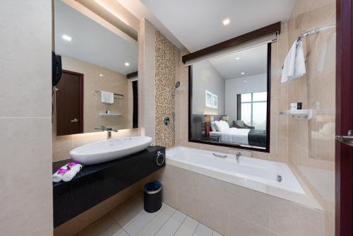 a bathroom with a sink and a tub and a bed at Raia Hotel & Convention Centre Kuching in Kuching