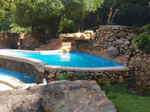 a swimming pool with a stone wall around it at El Shadai Guest House & Spa Hartbeespoort in Hartbeespoort