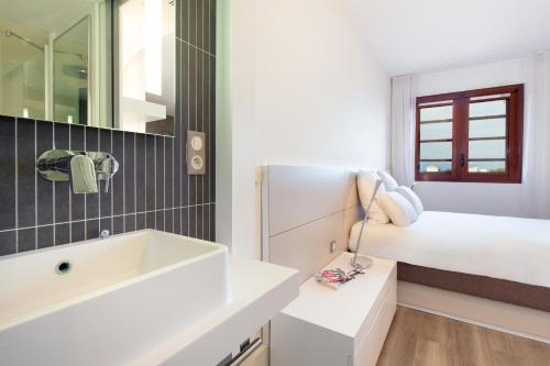 - une salle de bains blanche pourvue d'un lavabo et d'un lit dans l'établissement Novotel Suites Perpignan Centre, à Perpignan