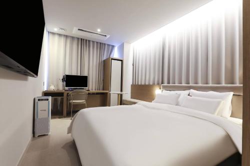a bedroom with a large white bed and a desk at Wonju Brown Dot Hotel Corporate city in Wonju
