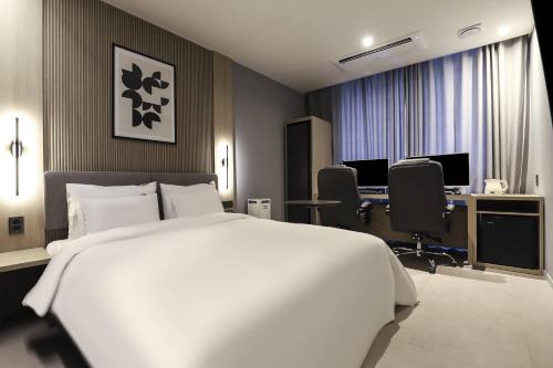 a bedroom with a large white bed and a desk at Wonju Brown Dot Hotel Corporate city in Wonju