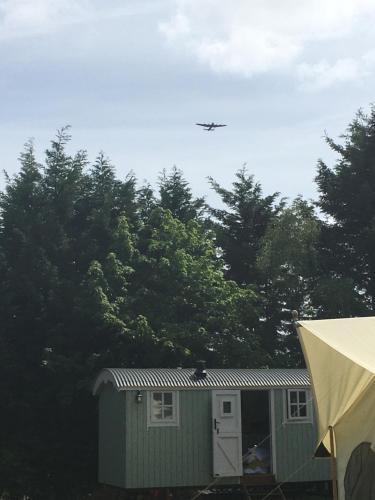 an airplane flying over a green building with trees at Jasmine The Shepherd Hut in Woodhall Spa