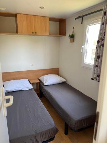 deux lits dans une petite pièce avec une fenêtre dans l'établissement Bungalow à l'asinerie, à Jau-Dignac-et-Loirac