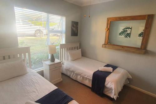 1 dormitorio con 2 camas, espejo y ventana en Sunny 2 bedroom apartment on stunning golf course, en Plettenberg Bay