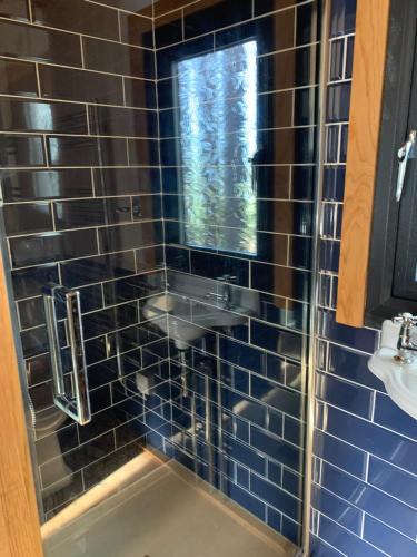 ducha de azulejos azules con lavabo y ventana en Cosy Shepherd's Hut near Shrewsbury, 