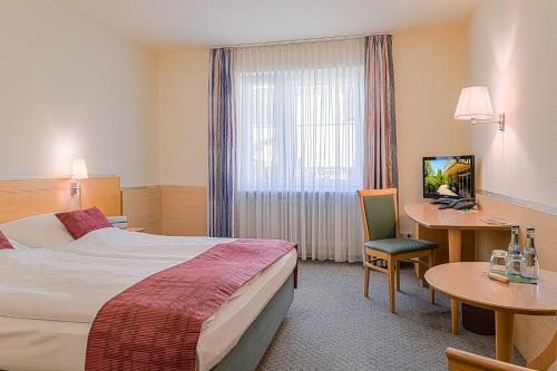 a hotel room with a bed and a desk and a tv at Hotel Am Moosfeld in Munich
