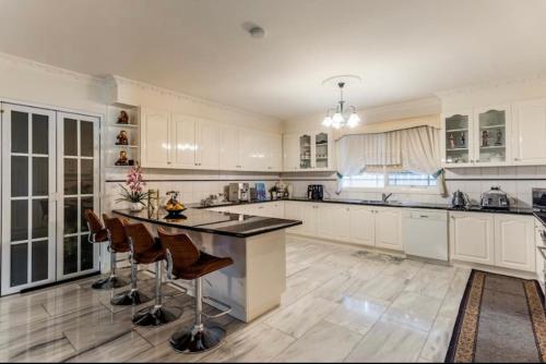a large kitchen with white cabinets and a island with bar stools at Cosy private room easy access to city & airport in Melbourne