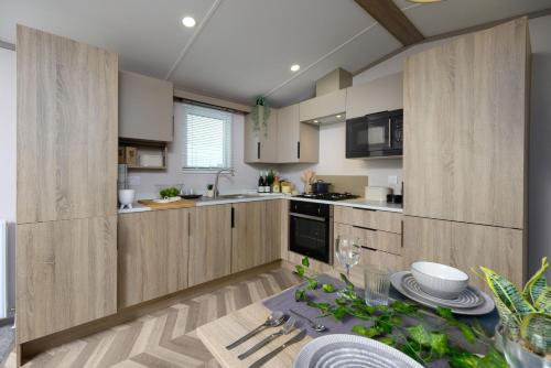 a kitchen with wooden cabinets and a table with plates at Stonewood Premium - 2 bedroom VS04 in Tenby
