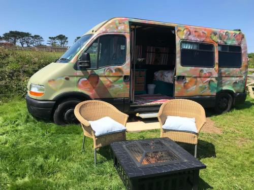a van parked in a field with two chairs and a table at Berty the campervan in Carbis Bay