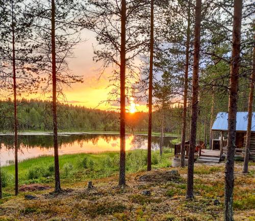 a sunset over a lake with a cabin at Glamping Laenlammen tila in Rovaniemi