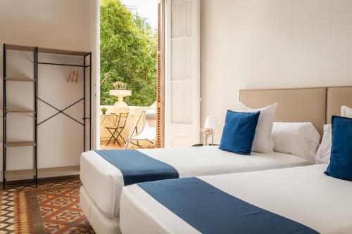 two beds with blue and white pillows in a room at Hotel Medium Sitges 1883 in Sitges