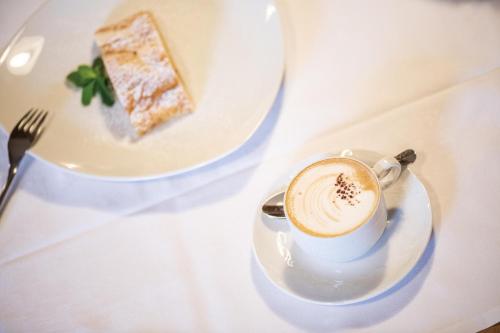 a cup of coffee on a plate with a piece of cake at Gasthof Teiser Stern in Funes