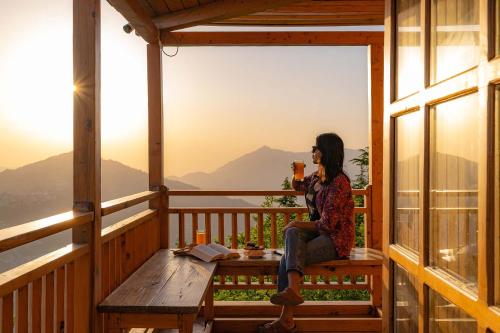 a woman sitting on a bench on a porch with a drink at StayVista at DAAFI House with Comp Breakfast in Theog