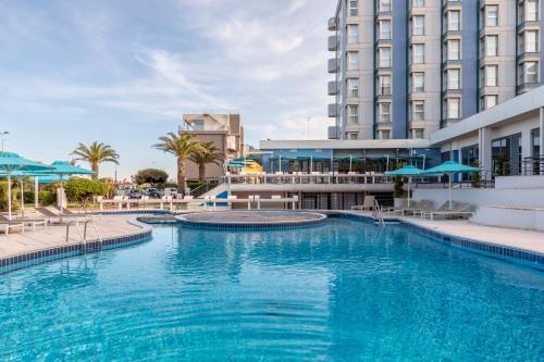 una grande piscina con acqua blu di fronte agli edifici di B&B Hotel Chioggia Airone a Sottomarina
