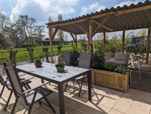 een patio met een tafel en stoelen en een houten pergola bij Huisje Hartenlust in Bodegraven