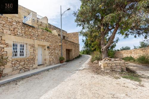 une route vide à côté d'un bâtiment en pierre avec un arbre dans l'établissement Peaceful, comfy 1BR Nature Retreat: Serene Bliss by 360 Estates, à Mġarr