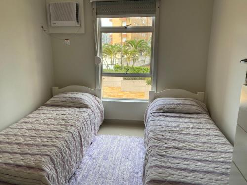 two beds in a room with a window at Apto todo equipado em Caiobá há 50m do mar in Matinhos