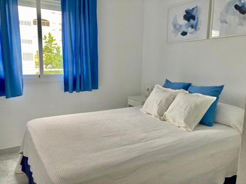 a bedroom with a white bed with blue curtains at APARTAMENTO GENOVEVA PLAYA - ValdelagranaCadizCom in El Puerto de Santa María