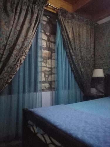 1 dormitorio con cortinas azules y 1 cama con lámpara en Αρχωντικα στην Τρiχονιδα, en Agrinio