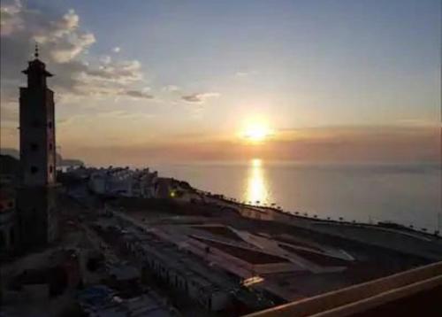 una puesta de sol sobre una ciudad con el océano y una torre del reloj en Résidence bades en Alhucemas