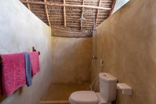 a bathroom with a toilet and towels on a wall at Paje Beach Bandas in Paje
