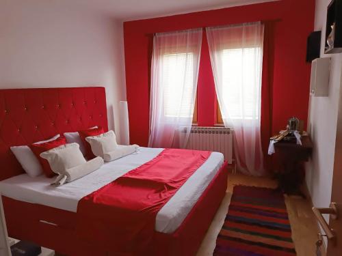 a red bedroom with a bed with a red headboard and two windows at Nera-etwa Konjic 1 apartment in Konjic