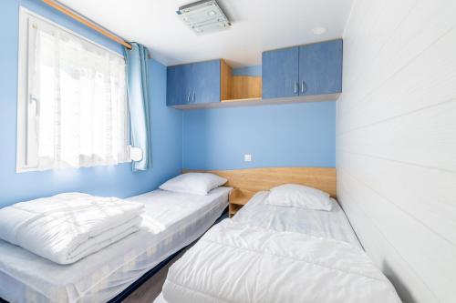 2 camas en una habitación con paredes azules y ventana en Mobil home Le Denver, en Noyelles-sur-Mer