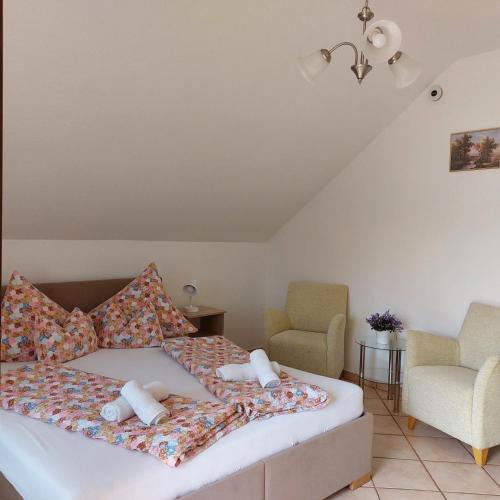 a bedroom with a bed with pillows and two chairs at Erika Apartmanházak in Hévíz