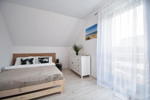 biała sypialnia z łóżkiem i oknem w obiekcie Domki Lilia Sarbinowo w Sarbinowie