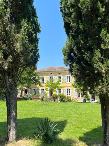 une grande maison jaune avec des arbres devant elle dans l'établissement Villa Toscane créations à 20 mn de Toulouse, à Azas