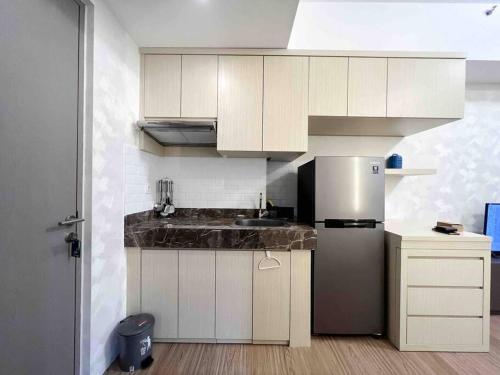 a kitchen with white cabinets and a stainless steel refrigerator at Apt Vasanta Innopark Studio Latte dgn Bathub & Pool Ch3n in Jarakasta