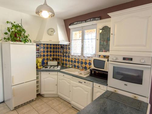 une cuisine avec des armoires blanches et un réfrigérateur blanc dans l'établissement Maison de plain-pied avec jardin, clim, 3 chambres et parking près du Bassin de Thau - FR-1-604-19, à Mèze