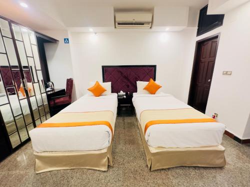 two beds in a room with white walls and orange pillows at The Elite Residence Dhaka in Dhaka