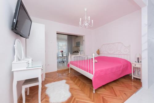 a white bedroom with a pink bed and a tv at Apartmani Antunović Podgora in Podgora