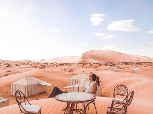 a woman sitting at a table in the desert at Desert Paradise Luxury Camp in Merzouga