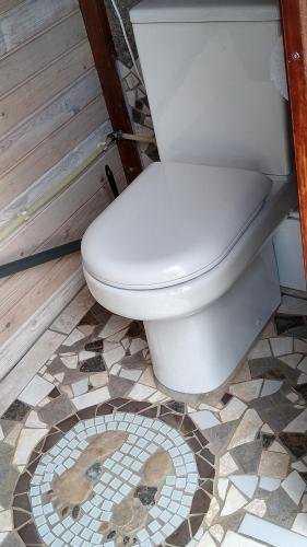 a toilet in a bathroom with a tile floor at Cosy Farmhouse Glamping in Stege