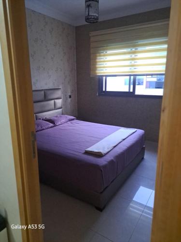 ein Schlafzimmer mit einem Bett mit violetter Bettwäsche und einem Fenster in der Unterkunft Blanca beach in Sidi Rahal