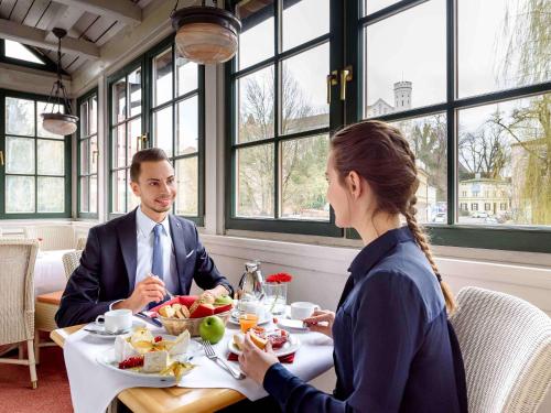 Un uomo e una donna seduti a tavola mangiando cibo di Mercure Hotel München Airport Freising a Freising
