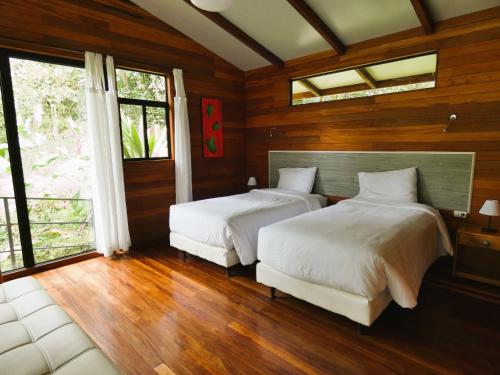 two beds in a room with wooden walls and windows at San Isidro Lodge in Cosanga