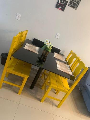 a black table with yellow chairs and a vase of flowers at Aconchego do Vale in Blumenau
