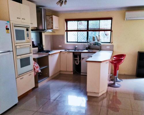 a kitchen with white appliances and a red stool at Aspley property in Brisbane