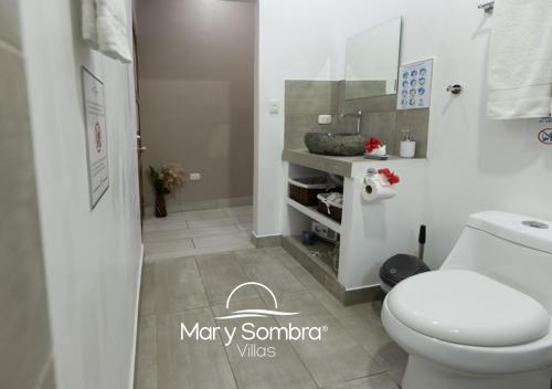 a white bathroom with a toilet and a sink at Mar y Sombra Villas in Quepos
