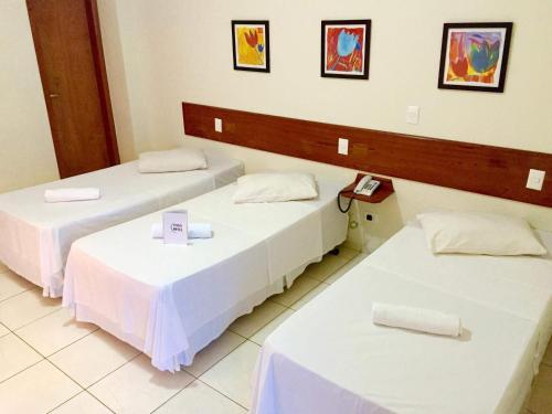 two beds in a room with two tables at Turis Hotel Centro in Campo Grande