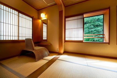 an empty room with a chair and two windows at Shima-Onsen Toshimaya in Nakanojo