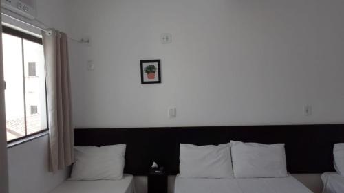 a bedroom with a bed with white pillows and a window at Hotel Pousada Santa Maria in Aparecida
