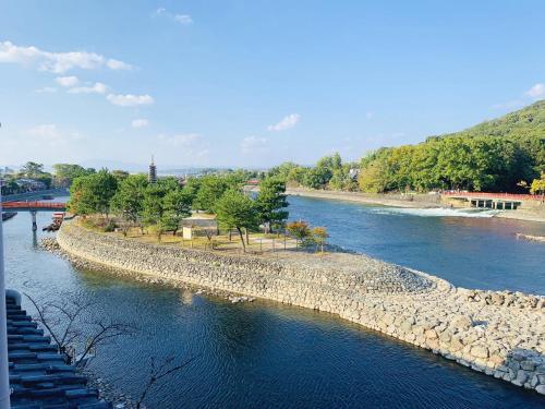 a river with a rocky shore and a bridge at Hanayashiki Ukifune-en in Uji